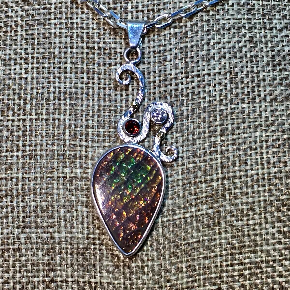 Canadian Ammolite (ammonite) Pendant, with Idaho garnet, White Sapphire, set in Sterling/Fine Silver/18K Gold.
https://dancing-raven-stoneworks-llc.square.site/product/drs-19-206-19-collection-fossil-ammonite-pendant/90?cs=true